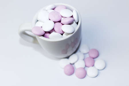 Full cup of pink and white peppermint candies on a white background