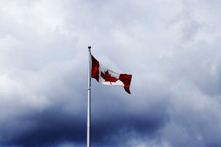 Canadian flag on a flagpole with a dramatic cloudsの写真素材