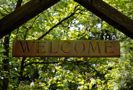 Wooden welcome sign hanging in front of green treesの写真素材