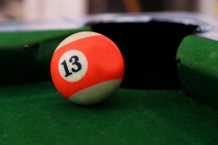 Pool ball number 13, as known as lucky number, in front of hole on green billiard tableの写真素材