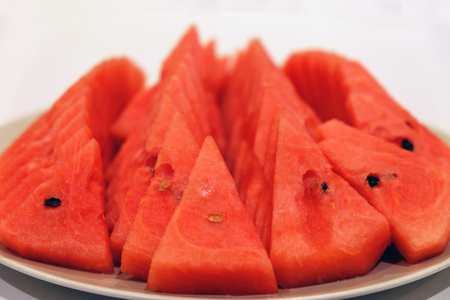 Sliced juicy red watermelon with seeds on the white round dish and white backgroundの写真素材