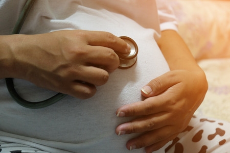 Asian pregnant woman holding her own belly and using stethoscopes listening to the baby insideの写真素材