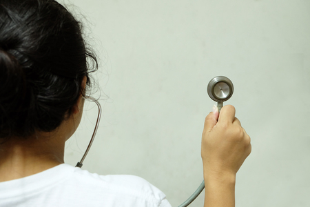 Back side of Asian woman who is holding, lifting and listening the medical stethoscopes with white backgroundの写真素材