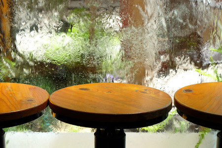 Round wood chairs with the background of falling water on the transparent glass window