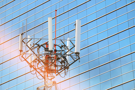 Cellular network antenna with background of windows of high building and beautiful sunlightの写真素材