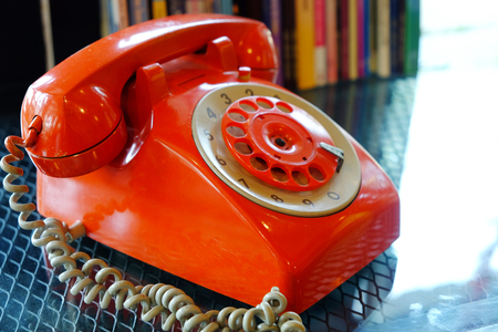 Closeup old fashioned fixed line orange rotary phone on glass tableの写真素材