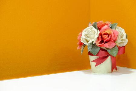 Plastic flower in a vase on white table at the corner with orange wall background and copy space areaの写真素材