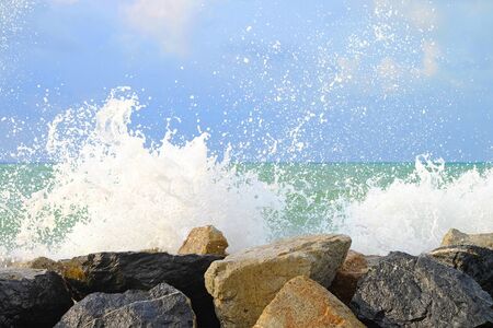 Water wave hit stone wall and made instant bubble foam on the shoreの写真素材