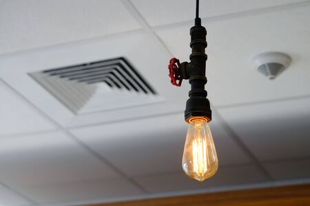 Vintage filament lamp in design of metal water pipe valve, hanging from the white ceiling