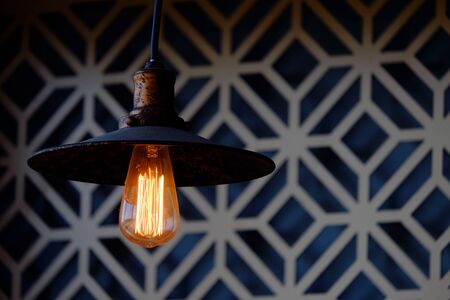 Vintage filament lamp with glowing tungsten in hat shape lantern, hanging from ceiling