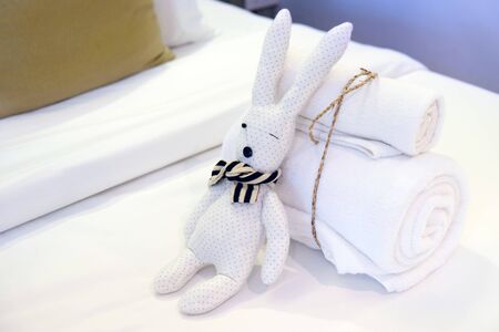 Roll of towels tied by rope, and rabbit doll on white bed sheet prepared for welcome visitor of hotel or resortの写真素材