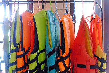 Many colorful life jackets hanging on the cloth rackの写真素材
