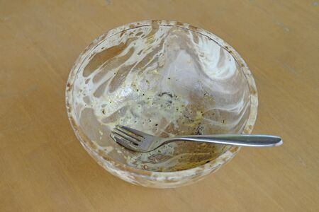 Finished and empty salad with dressing, in coconut shell bowl and a metal fork, on wood tableの写真素材