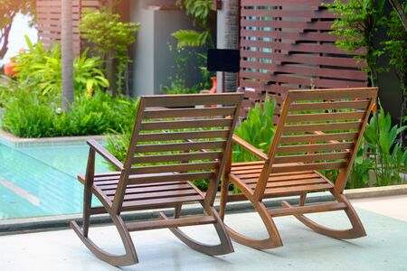 Empty wood rocking chairs at balcony near swimming pool