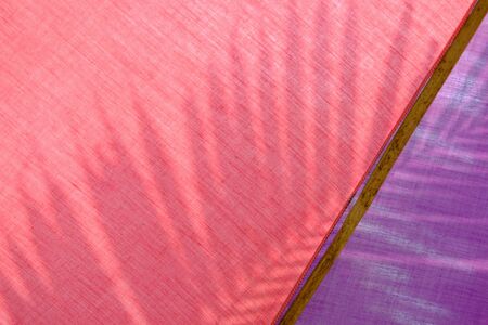 Colorful red and purple fabric panel of umbrella with shadow of young coconut leaf