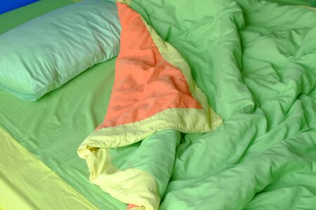 Unmade bed with green pillow and blanketの写真素材
