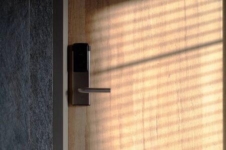 Metal doorknob on closing wooden door with sunlight and shadow
