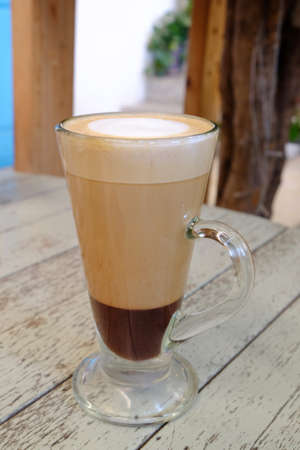 Hot mocha drink served in chocolate and coffee layers, in tall glass with handler on old wood...