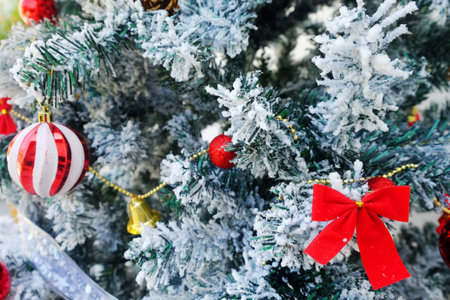 Closeup of snowy Christmas green tree, decorated by red ribbon and balls