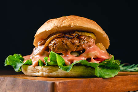 Fresh tasty chicken burger on wood table. Sandwich with chicken burger, tomatoes, pickled cucumber and fried egg. Fresh tasty chicken burger on wooden table.の写真素材