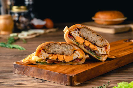 Fresh tasty chicken burger on wood table. Sandwich with chicken burger, tomatoes, pickled cucumber and fried egg. Fresh tasty chicken burger on wooden table.の写真素材