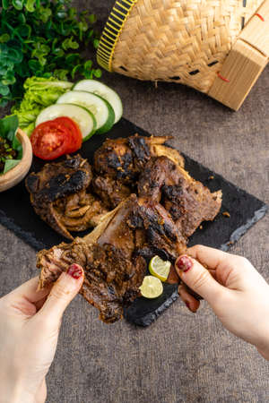 Ayam bakar or roasted chicken on banana leaf shoot at a rustic wooden background. Ayam bakar is a indonesian dish. Ayam bakar literally means "roasted chicken", in the smoky burning process.の写真素材