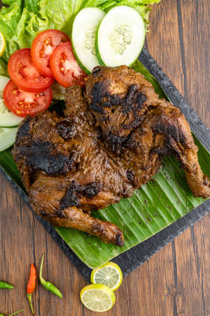 Ayam bakar or roasted chicken on banana leaf shoot at a rustic wooden background. Ayam bakar is a indonesian dish. Ayam bakar literally means "roasted chicken", in the smoky burning process.の写真素材