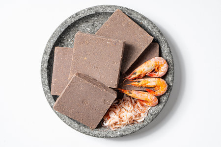 Traditional Indonesian Shrimp Paste Terasi on Mortal Stone isolated on white background, Fermented...