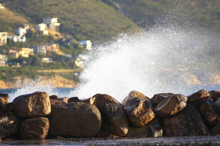 An ocean wave breaking over the stone harbour walkway with a plume of spray in late afternoon sunの写真素材