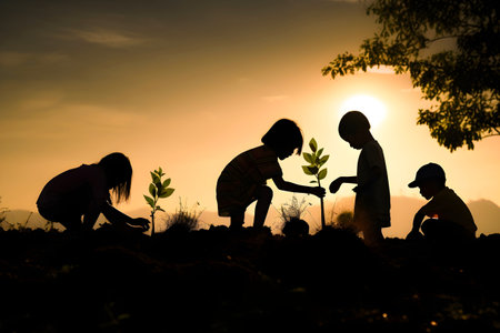 Silhouette of children planting trees in the garden at sunset.の素材