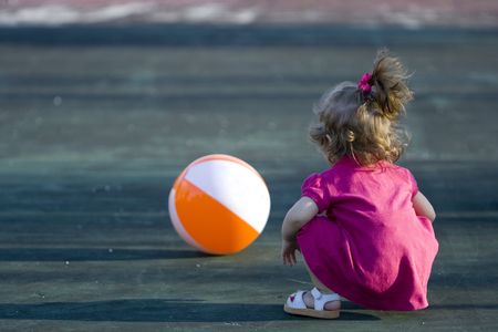 Little girl in a court playing with an orange and white beach ballの写真素材