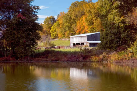 An old barn next to a pond with the autumn colors in the trees.の写真素材
