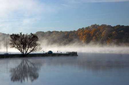 Foggy morning at the lake. A man sits in his truck watching the scene unfold before he begins to fish.の写真素材