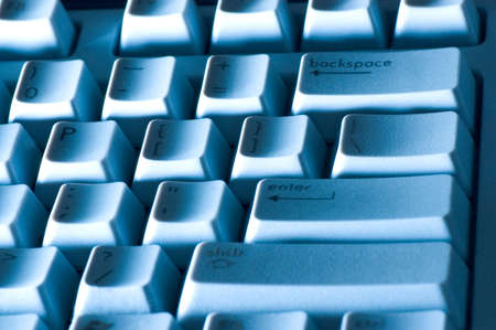 Close-up of a keyboard with a blue tone and dramatic lighting. The texture of the raised lettering on the slash key can be seen.の写真素材