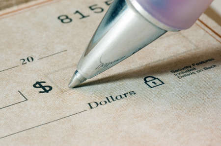 Close-up of a person filling out a dollar amount on a check, focus is sharp and on the pen tip and the dollar word and symbol.の写真素材