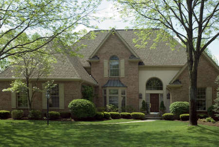 Beautiful brown brick home featuring a nice green lawn and formal landscaping.の写真素材