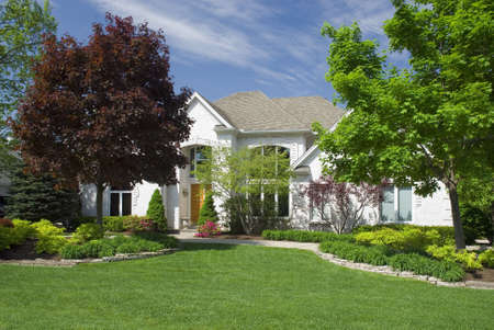 Beautiful white brick home featuring modern architectural styling and large windows with elaborate, colorful landscaping.の写真素材