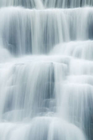 A close-up of a waterfall showing the smooth veil lines of the flowing and tumbling water. Given a...