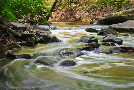 A beautiful cascade  with the golden tones of morning light on the water. Taken with  a slow shutter speed to smooth the water and show the movement as it twists and turns over the boulders. の写真素材