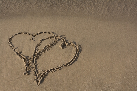Two intertwined hearts representing love drawn in the sand at a beach  の写真素材
