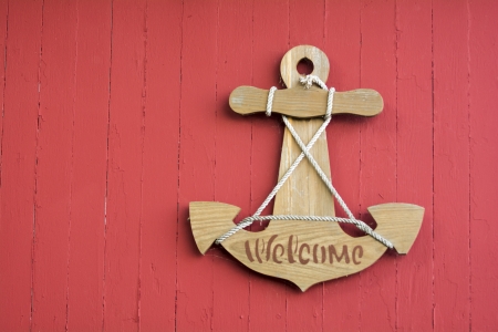 A wooden welcome sign in the shape of a boat anchor hanging on a red wood boat shed.の写真素材