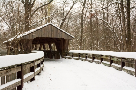 Winter scene with a winding wooden boardwalk leading to a covered bridge that crosses  a river in a wooded park. の写真素材