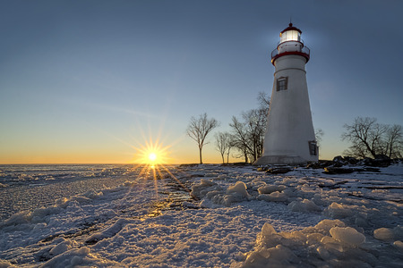 The historic Marblehead Lighthouse in Northwest Ohio sits along the rocky shores of the frozen Lake Erie. Seen here in winter with a colorful sunrise and snow on the ground.の写真素材