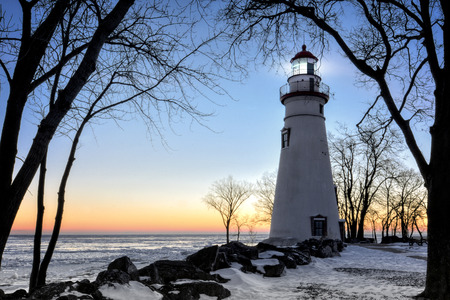 The historic Marblehead Lighthouse in Northwest Ohio sits along the rocky shores of the frozen Lake Erie. Seen here in winter with a colorful sunrise and snow on the ground.の写真素材