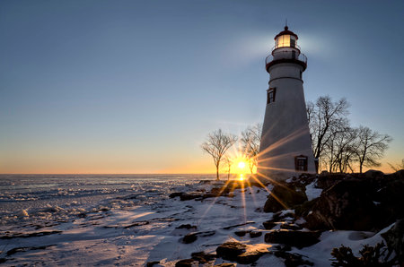 The historic Marblehead Lighthouse in Northwest Ohio sits along the rocky shores of the frozen Lake Erie. Seen here in winter with a colorful sunrise, snow on the ground.の写真素材
