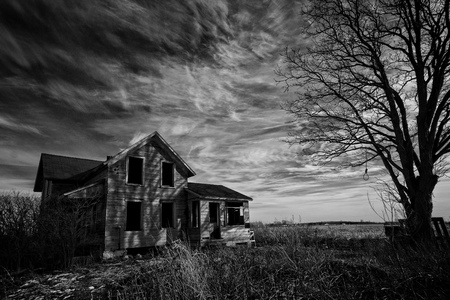 Black and white photo of an old scary abandoned farm house that is deteriorating with time with an old tree and a hangman's noose topped off with a dark sky.の写真素材