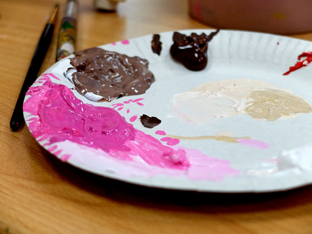 Simple white plate used as palette with some pink and brown paint in itの写真素材