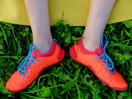 Woman legs in the red boots with a blue shoelaces on the grass and yellow plaid background