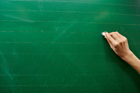 Right hand of a young girl holding white chalk ready to write on the big green school board backgroundの写真素材