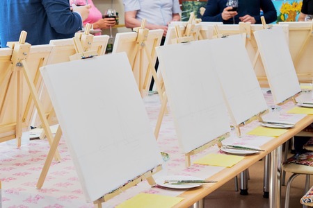 Canvases, brushes, palettes on the long wooden table ready for a masterclass in the art studio, people waiting to start drawingの写真素材